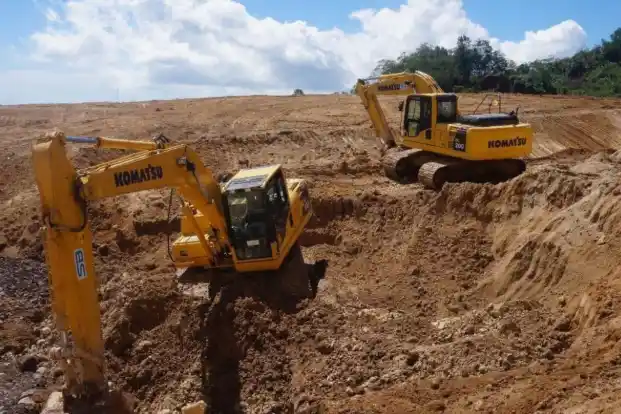 Dua unit excavator bekerja menggali dan memindahkan tanah di area proyek konstruksi.